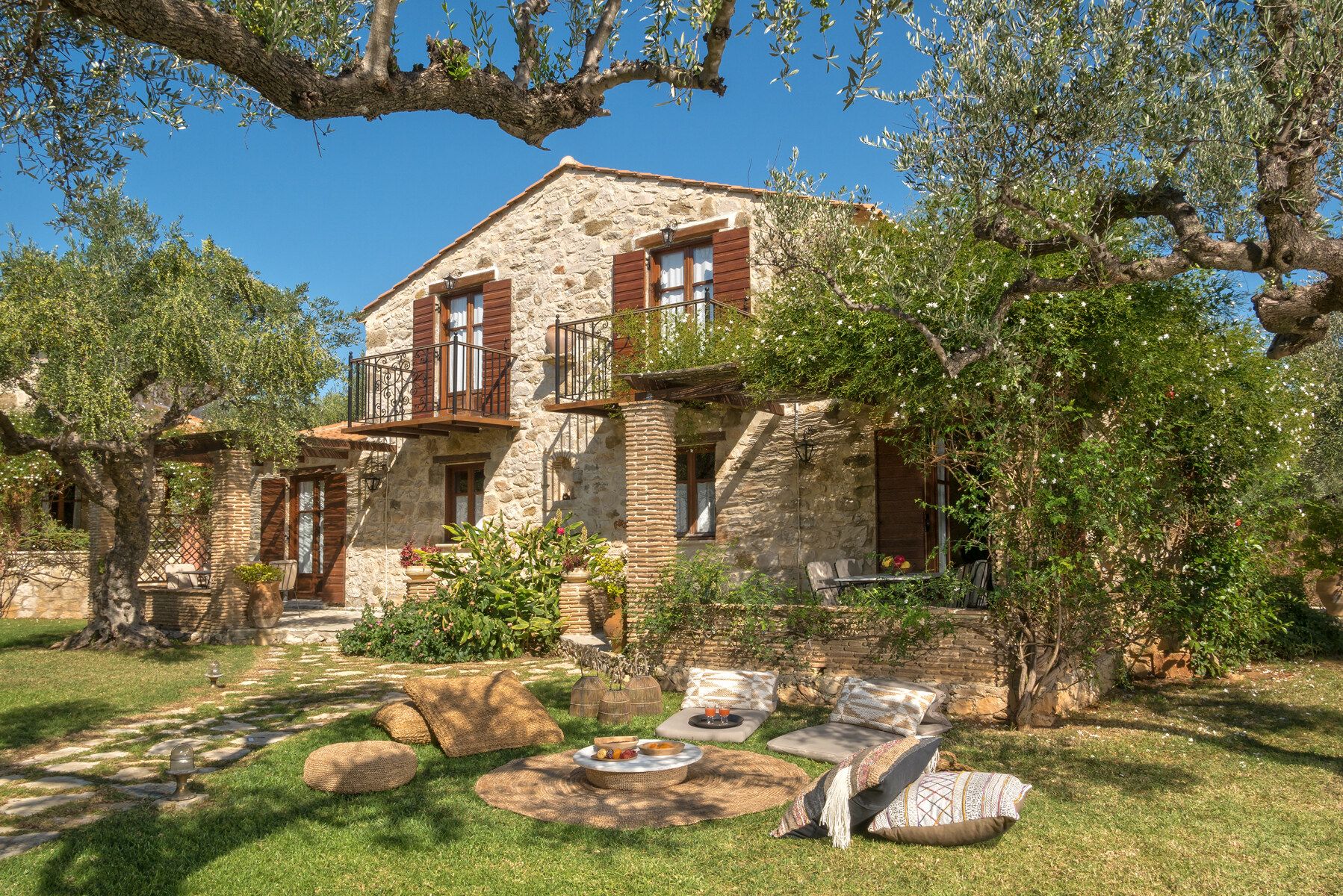 A stone house with wooden shutters behind old olive trees