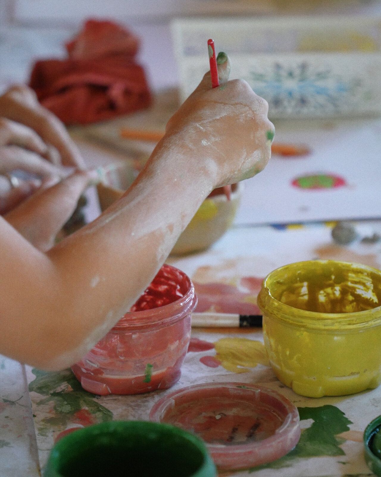 A hand painting a clay pot, between jars of colour