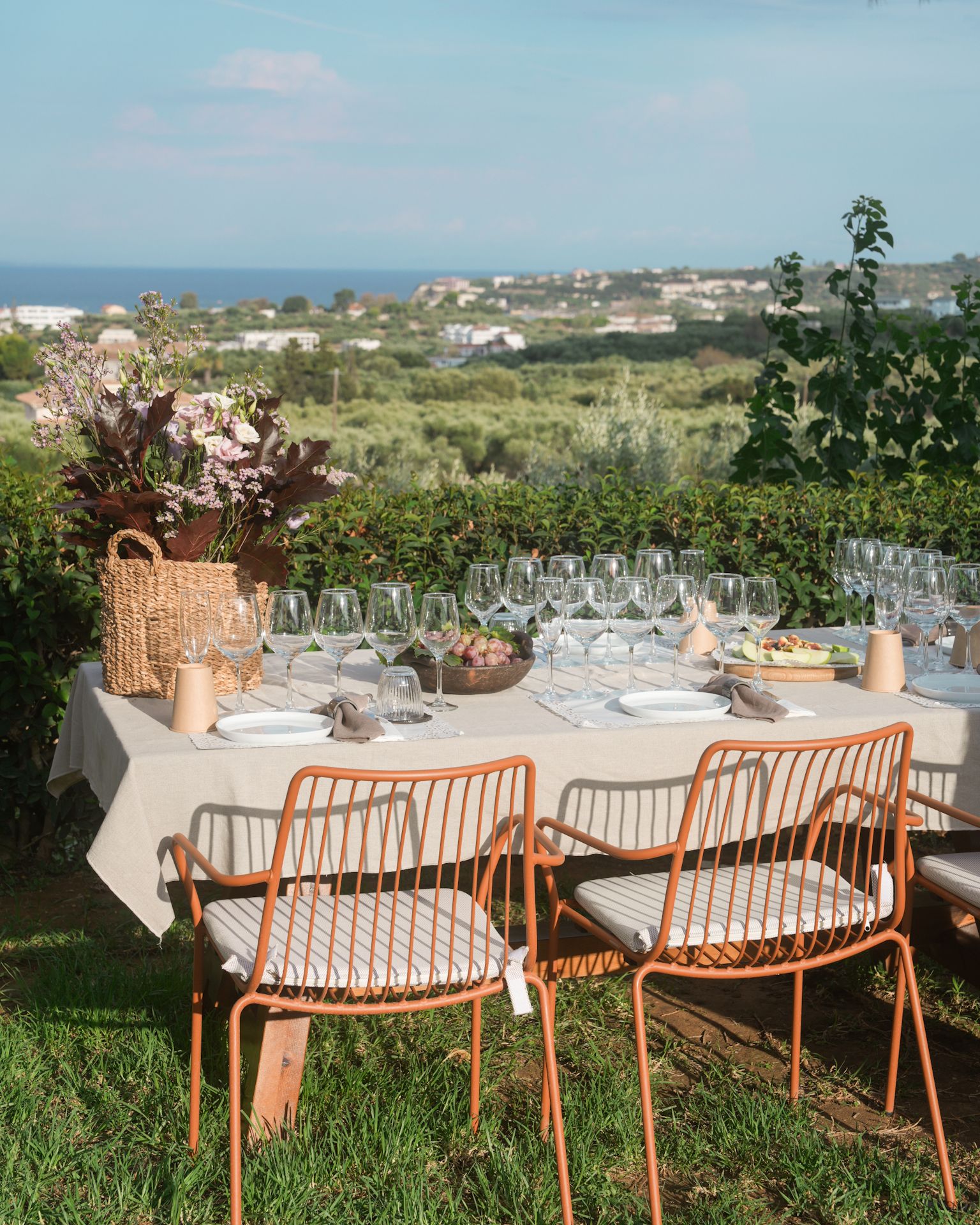 A long table set with wine glasses in the garden, overlooking the sea