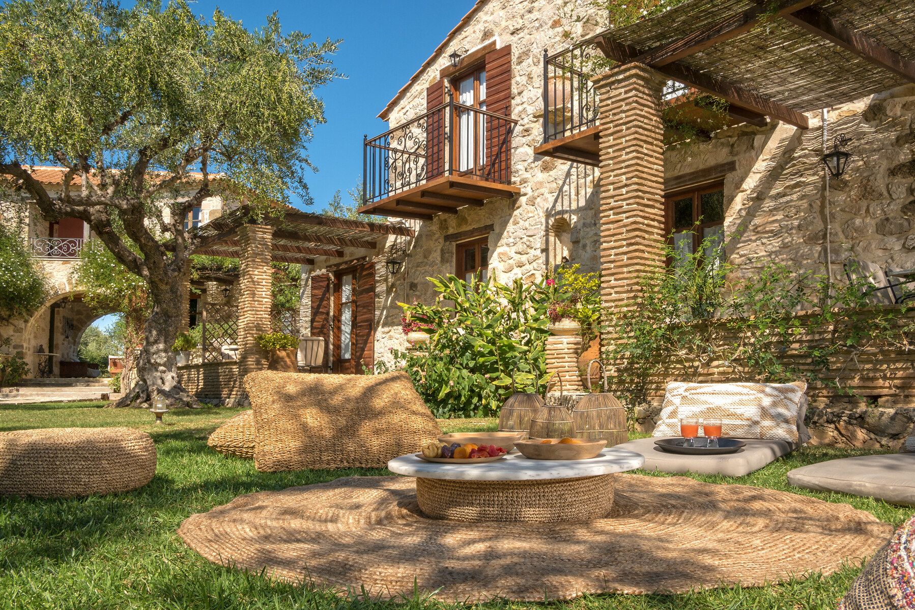 Cushions and a low table set on the grass in front of a stone house