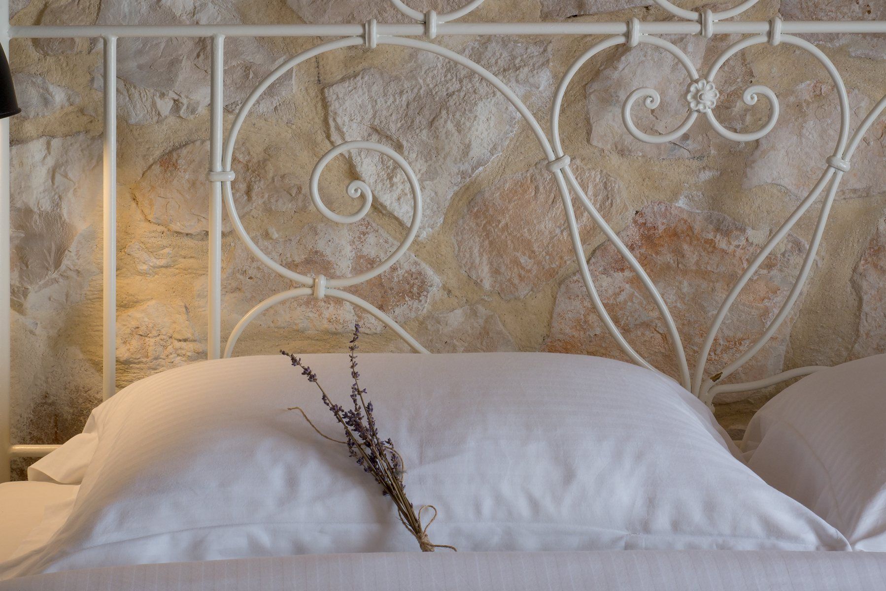 A bunch of dried lavender on a pillow, in front of an iron bed and a stone wall