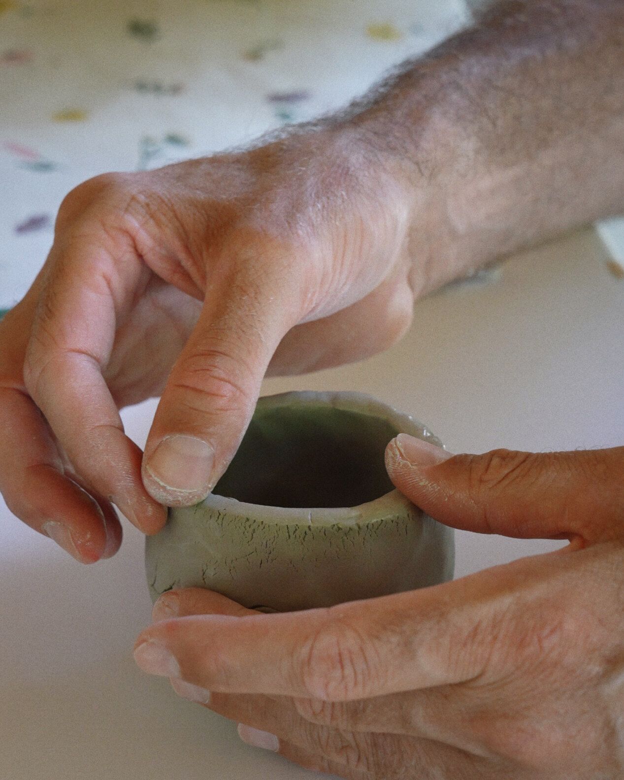 Hands shaping a small bowl of clay