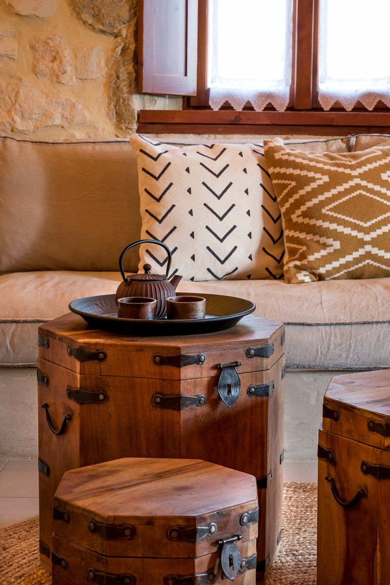 A clay teapot and cups on a tray, on old wooden chests in front of a sofa